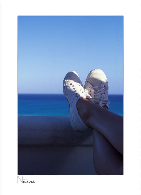 Frauenbeine in Turnschuhen, die auf einer Brüstung am Meer ruhen